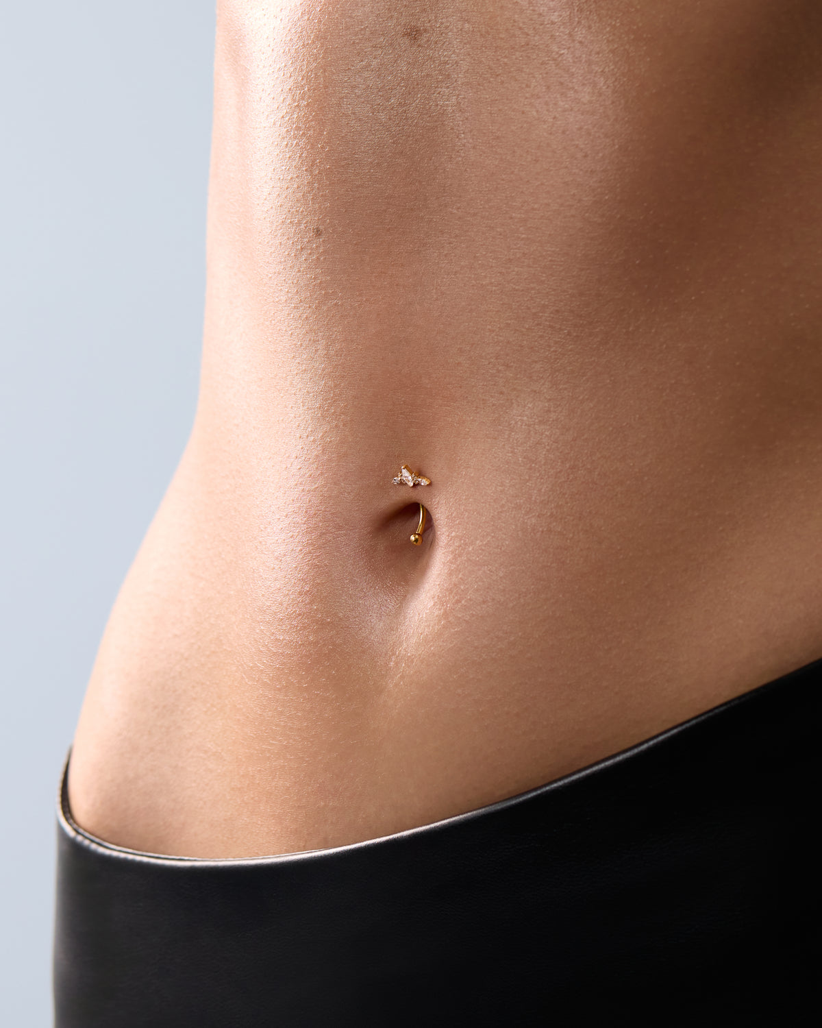 Piercing nombril doré orné d'un motif papillon sur peau nue, avec vêtement noir en bas de l'image