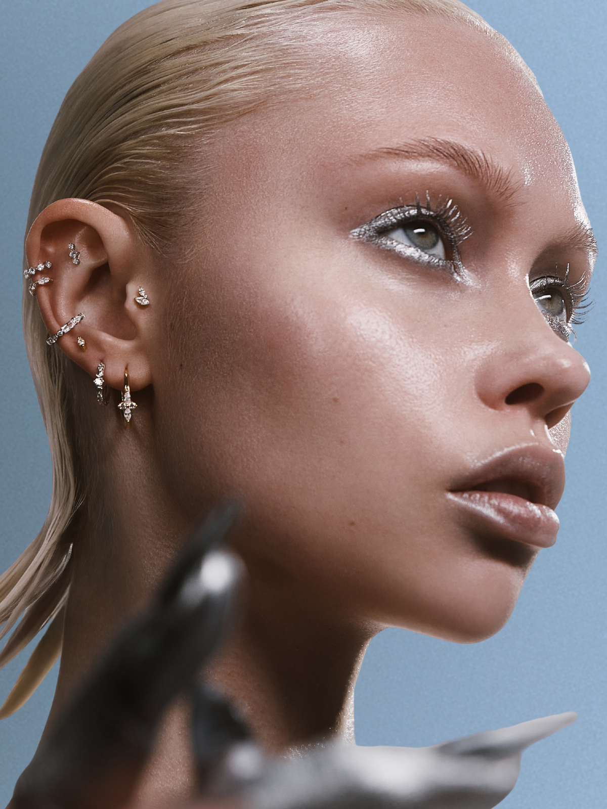 Portrait d'une femme blonde au visage tourné vers le haut, multiples piercings d'oreille sertis de pierres