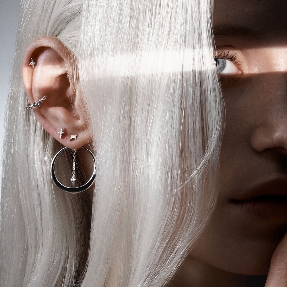 Gros plan sur une oreille percée au lobe, hélix et conch avec boucles d'oreilles et anneau créoles argentés