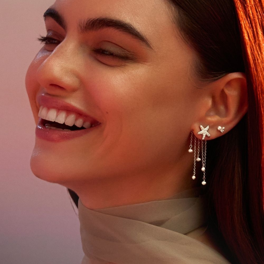 Portrait souriant d'une femme portant des boucles d'oreilles étoile, ligne perlée pendante et puce cœur au lobe et à l'hélix
