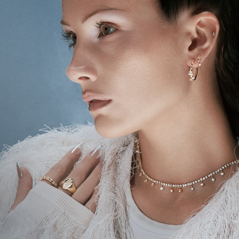 Femme en veste de plumes blanches portant créoles, bague et collier dorés, collection Snow