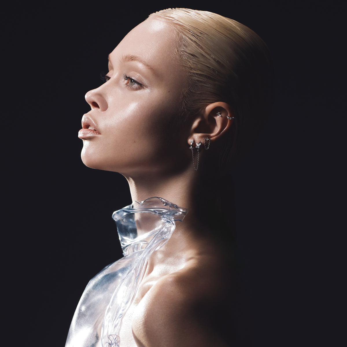 Profil de femme avec plusieurs piercings d'oreille à chaînes en titane et vêtement sculptural transparent sur fond noir