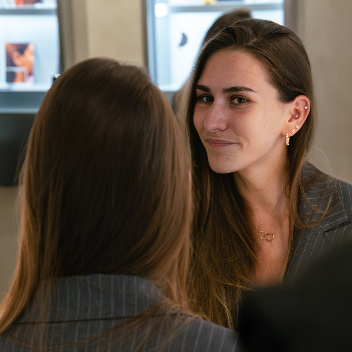 Portrait d'une jeune femme souriante portant des boucles d'oreilles et un collier, en conversation avec une autre personne