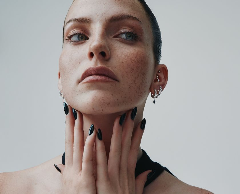 Portrait de femme aux taches de rousseur avec plusieurs piercings et boucles d'oreille pendantes